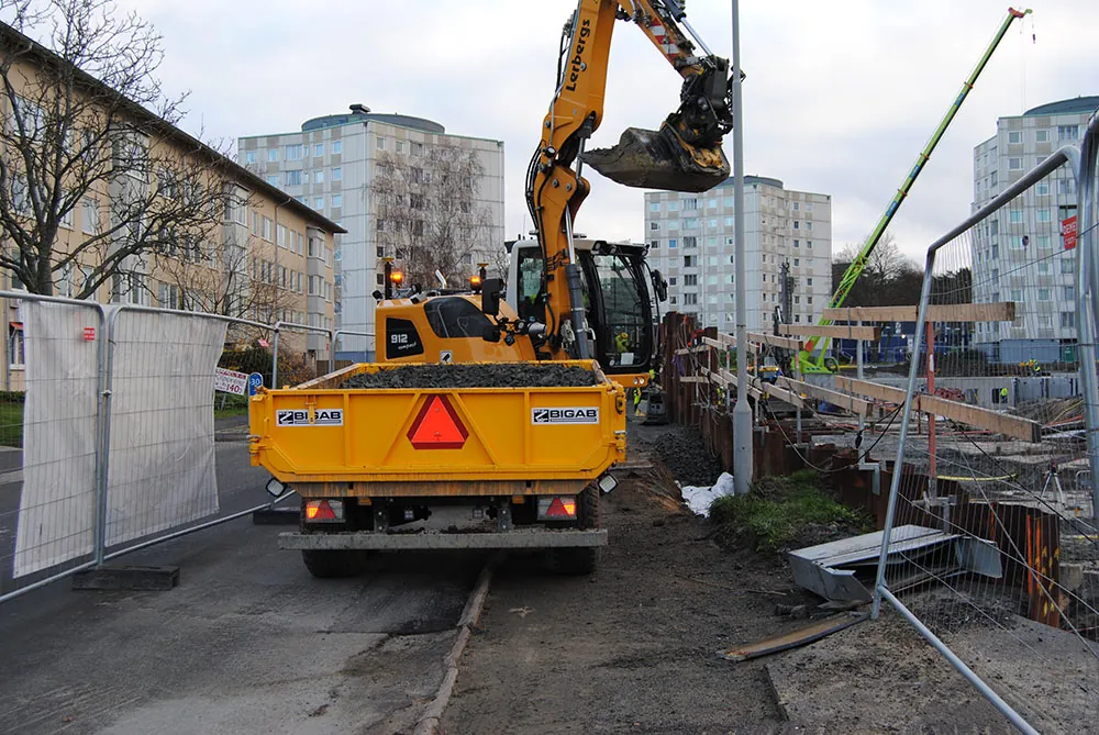Grävmaskin med förare utför markarbete vid bostadsområde i Göteborg